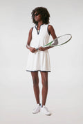A woman in a Tnuck Sport white and navy tennis dress with sneakers holds a racket, showcasing sporty style.